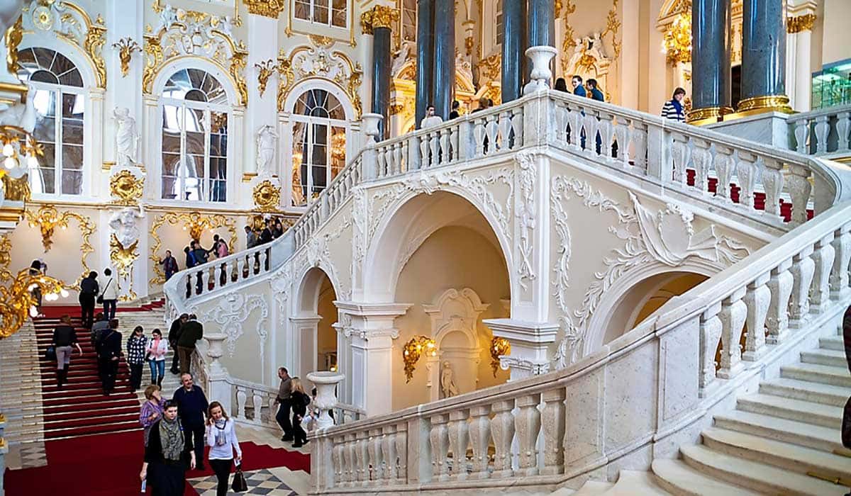 foto interna do museu Hermitage com escadas na cor branca e paredes brancas e douradas , viagem a rússsia