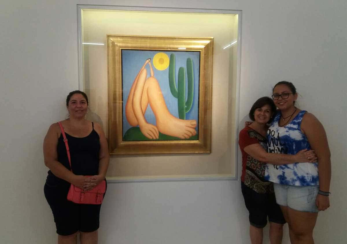 Pintura de um homem de pernas gordas e longas com cabeça de sol e um cacto ao fundo