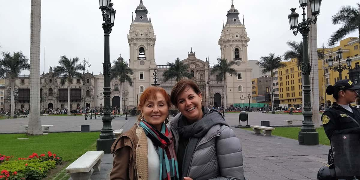 2 mukheres numa praça com uma igreja branca ao fundo e o céu nublado, 