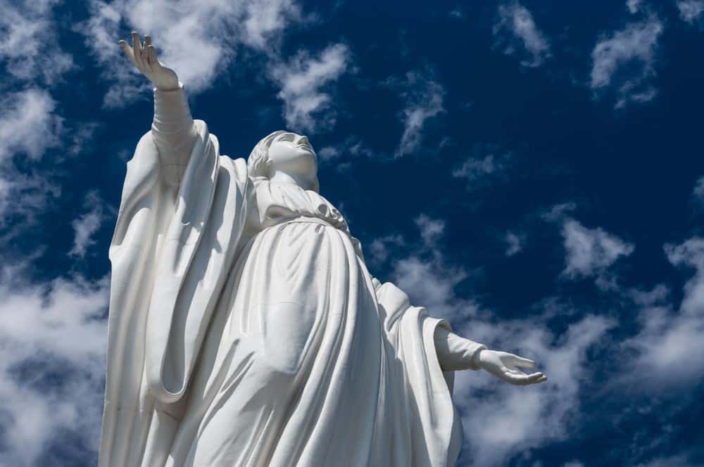 Imagem de santa em escultura branca e o céu azul com nuvens brancas