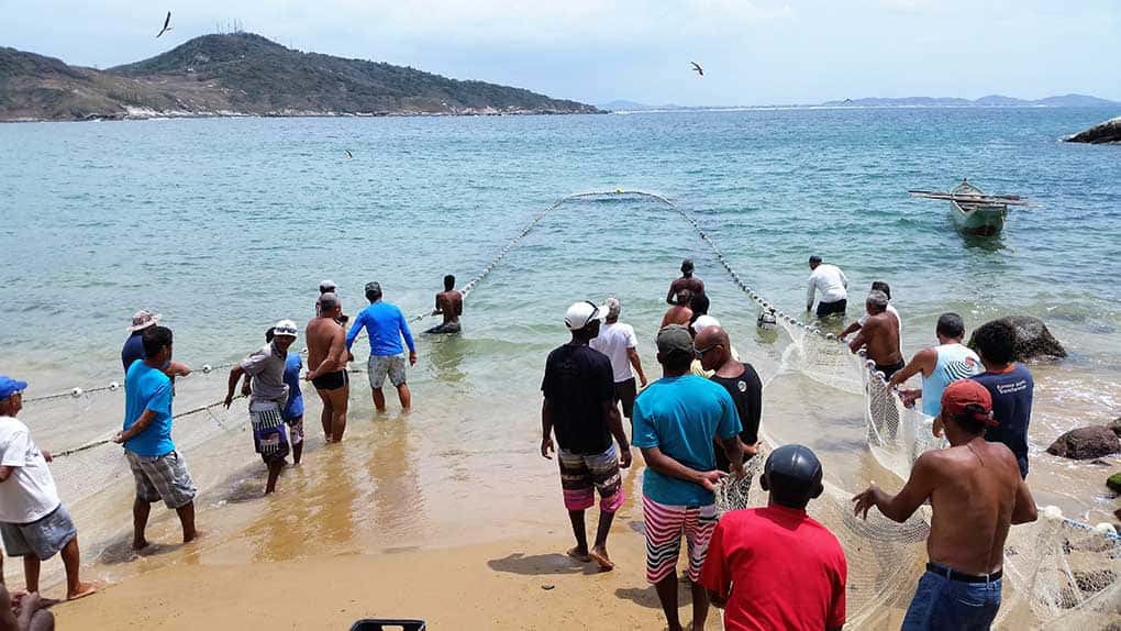 Homens e mulheres ajudando a puxar a rede em arrastão de peixe na Praia da Graçainha uma das praias de Arraial do Cabo