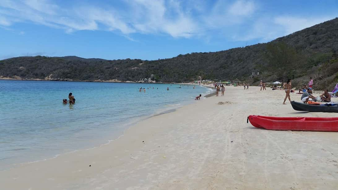 Praia do Forno, uma das praias de Arraial do Cabo, com faixa de areia, mar, pessoas e morros ao fundo