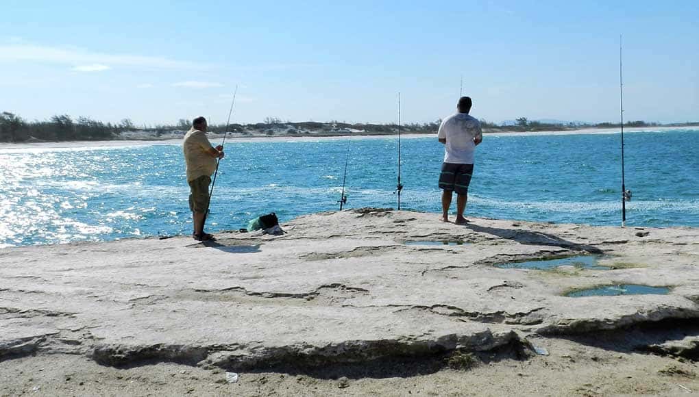 Pescadores pescando na pedra e vista da praia do Pontal, uma das praias de Arraial do Cabo