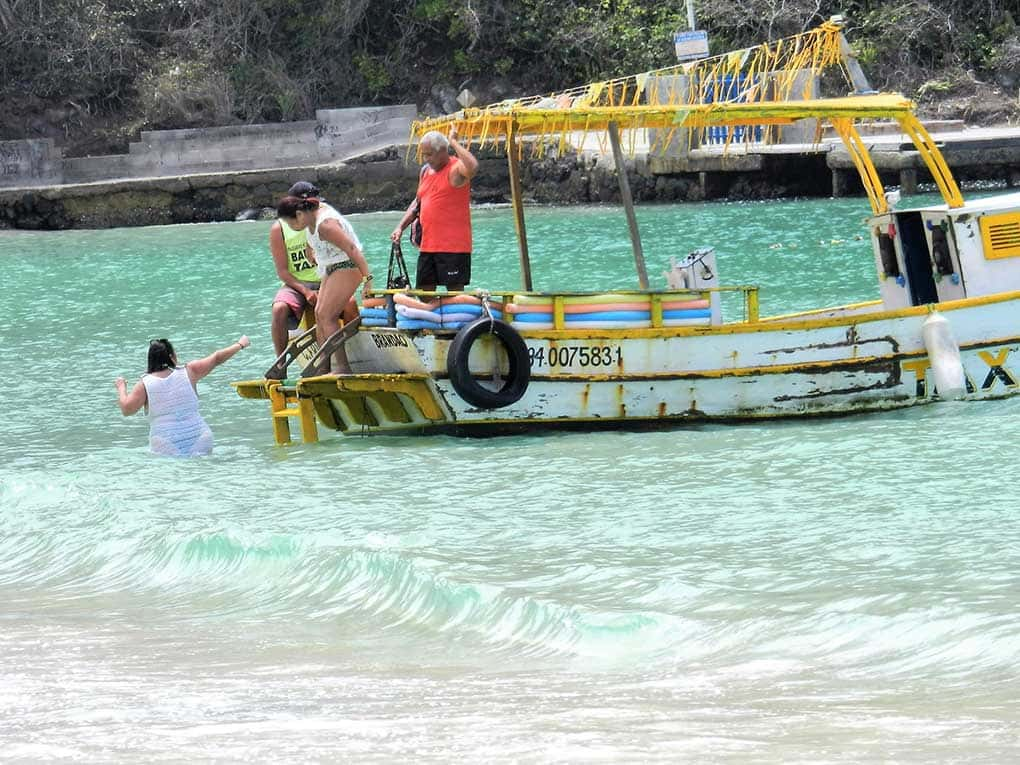 Barco com pessoas e uma pessoa subindo no barco. Chama-se barco-táxi e faz o transporte entre as praias de Arraial do Cabo