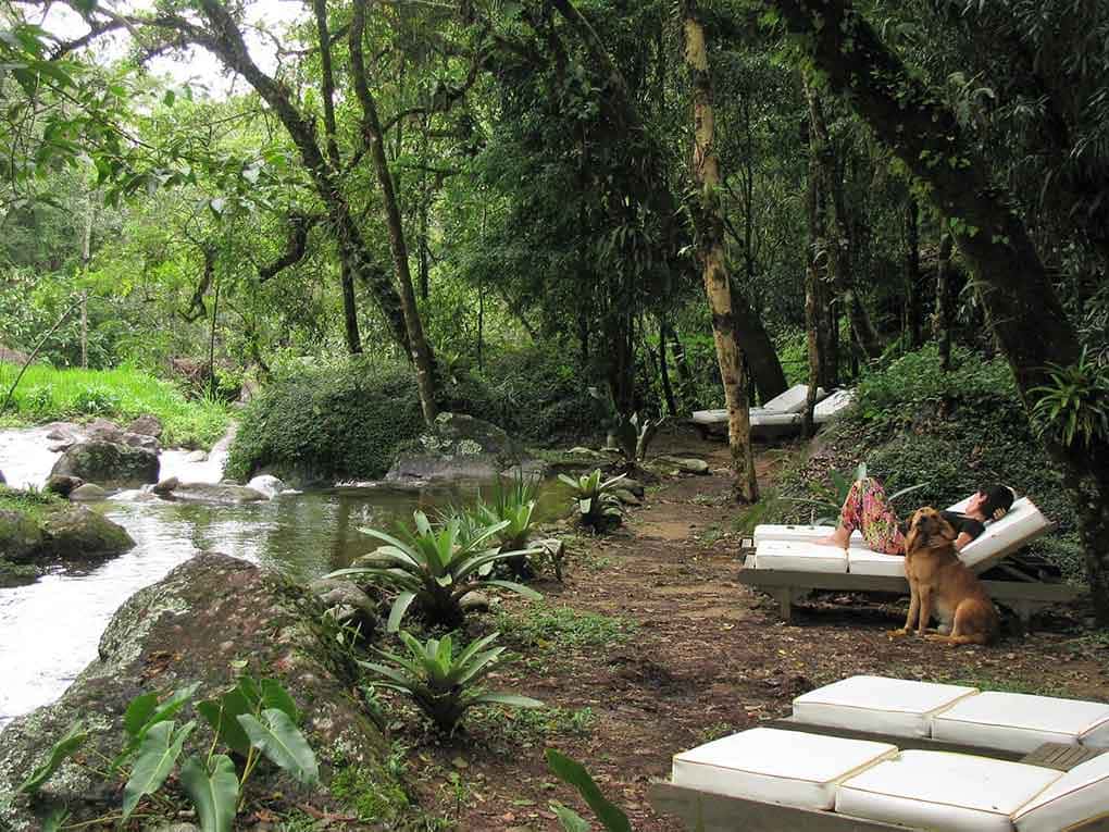 Moça e cachorro descansam à beira do rio em uma das pousadas em Visconde de Mauá