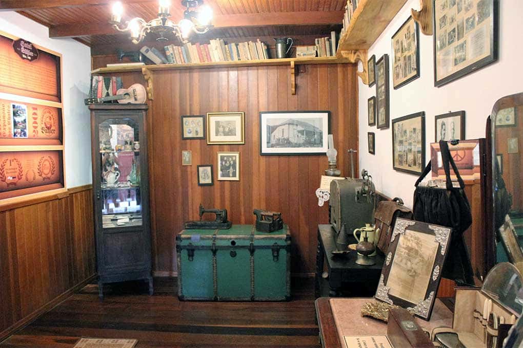 Sala com objetos variados: um baú, fotografias antigas, cofres etc, em uma das pousadas em Visconde de Mauá