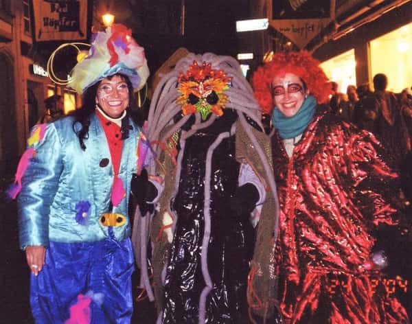Duas mulheres fantasiadas e no meio uma figura mascarada no Carnaval de Lucerna, na Suíça