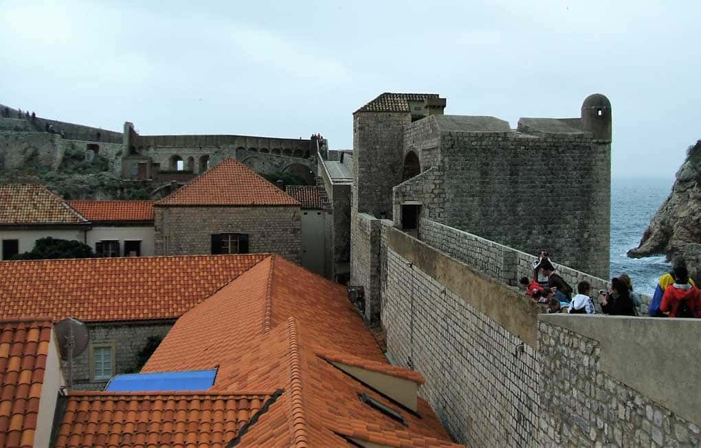 Pessoas andando por uma muralha e telhado de várias casas em Dubrovnik