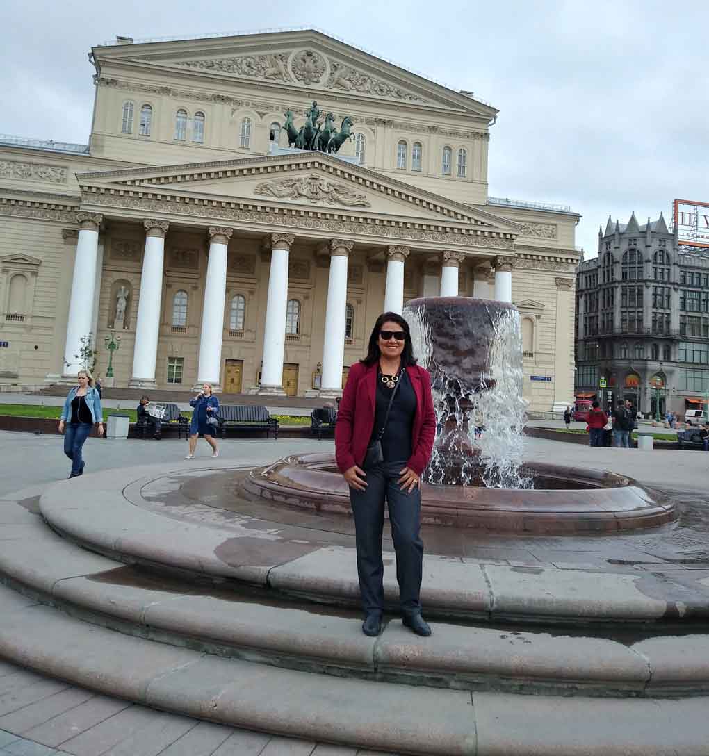 Cruzeiro na Rússia: mulher posa em frente a fonte de água e construção clássica com colunas, que é o Teatro Bolshoi, em Moscou